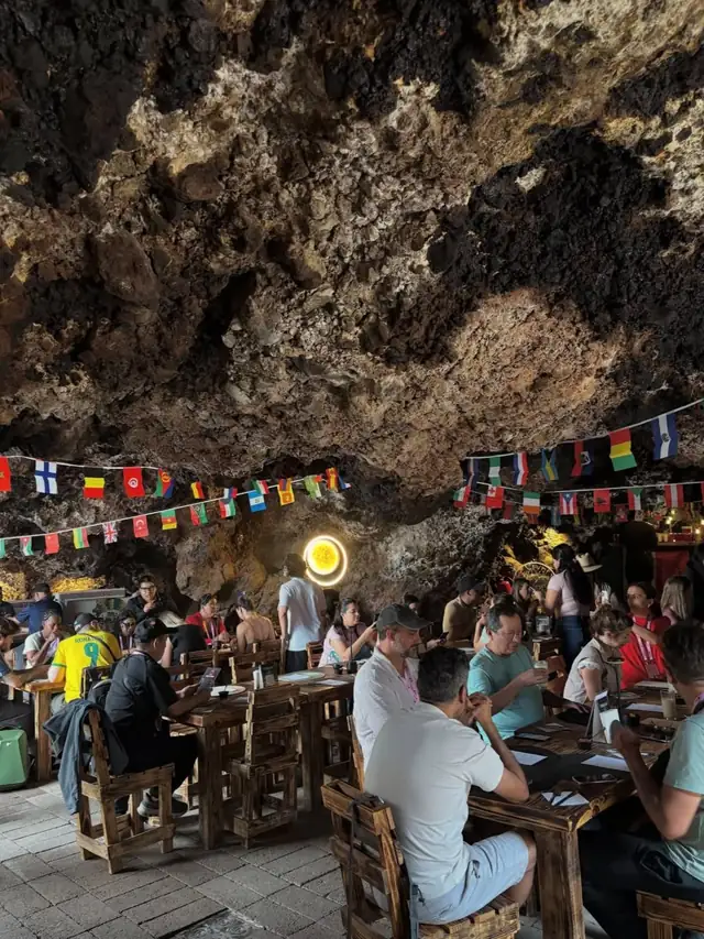 Comedor del restaurante dentro de la cueva, con mesas de madera y banderines bajo el techo de roca volcánica