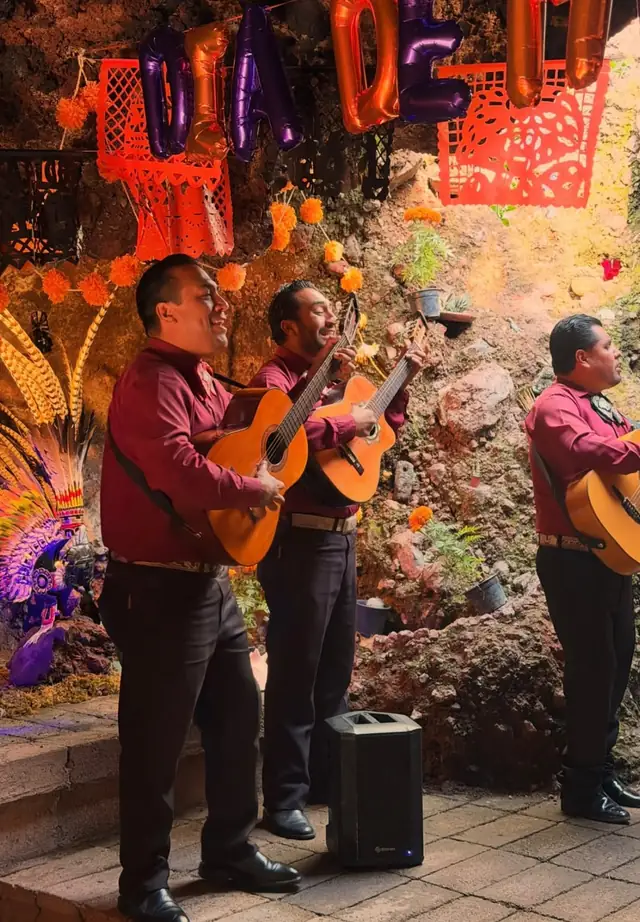 Mariachi tocando guitarras entre flores de cempasúchil y papel picado
