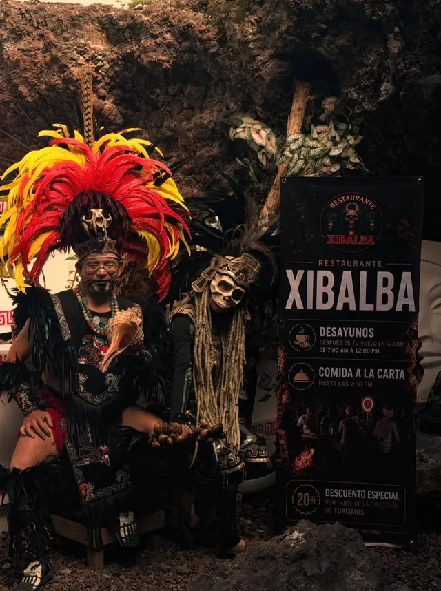 Danzantes con atuendos prehispánicos posando junto al cartel del restaurante